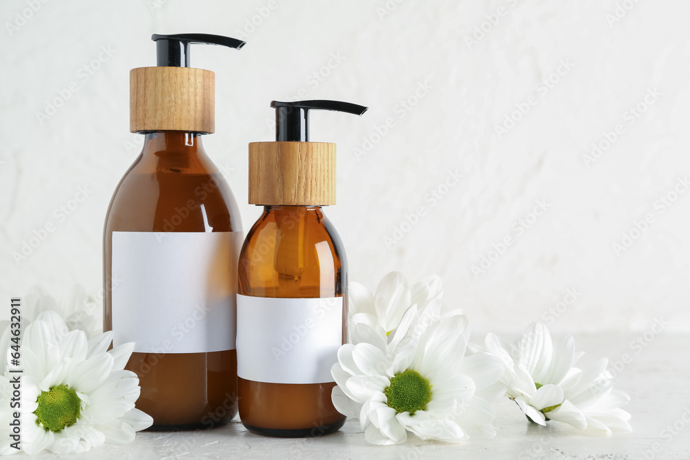 Bottles of cosmetic products and chamomile flowers on light background