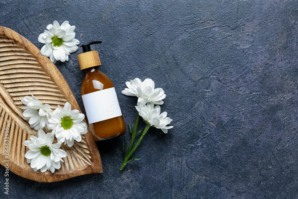 Composition with bottle of cosmetic product and chamomile flowers on dark background