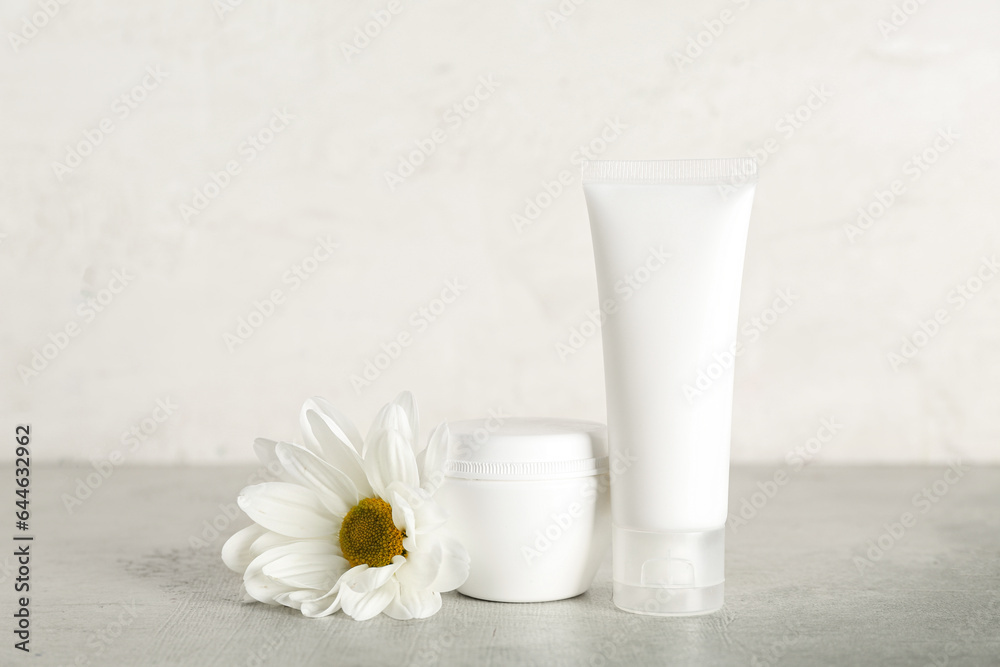 Cosmetic products and chamomile flower on table against light background