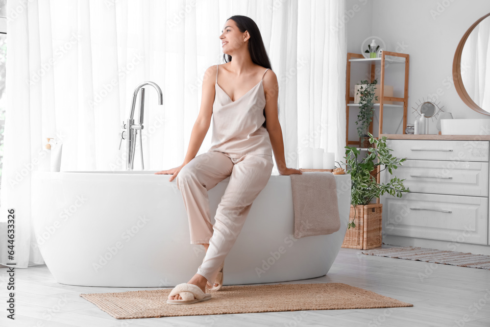 Young woman sitting on bathtub in bathroom