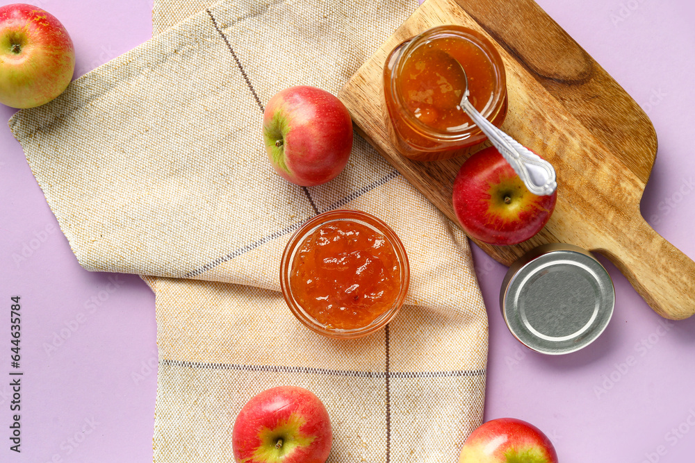 Wooden board with jar and glass bowl of sweet apple jam on purple background