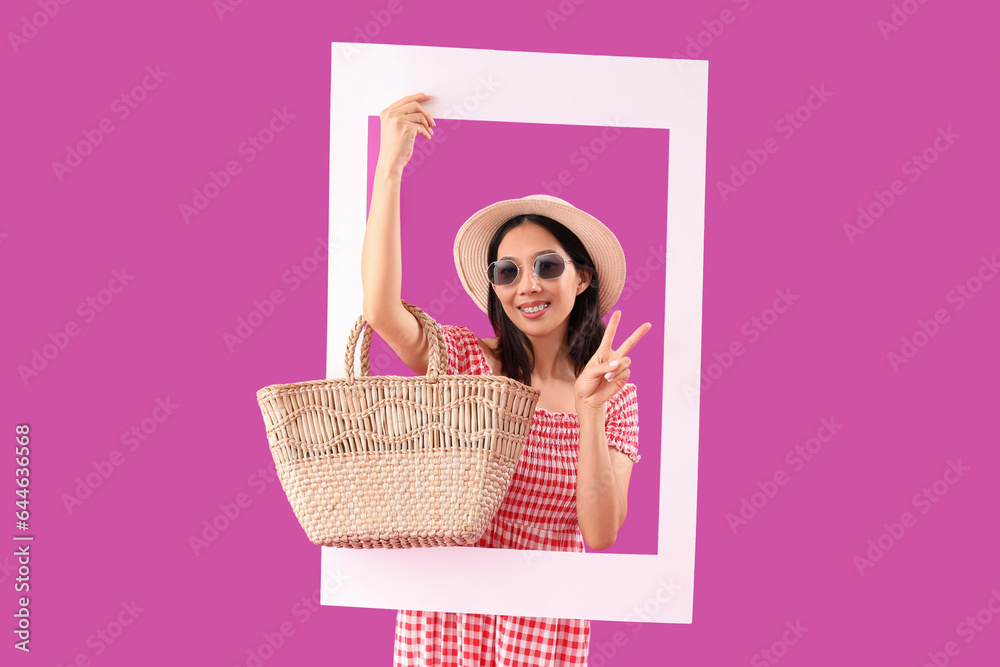 Stylish young beautiful Asian woman with frame showing victory gesture on purple background