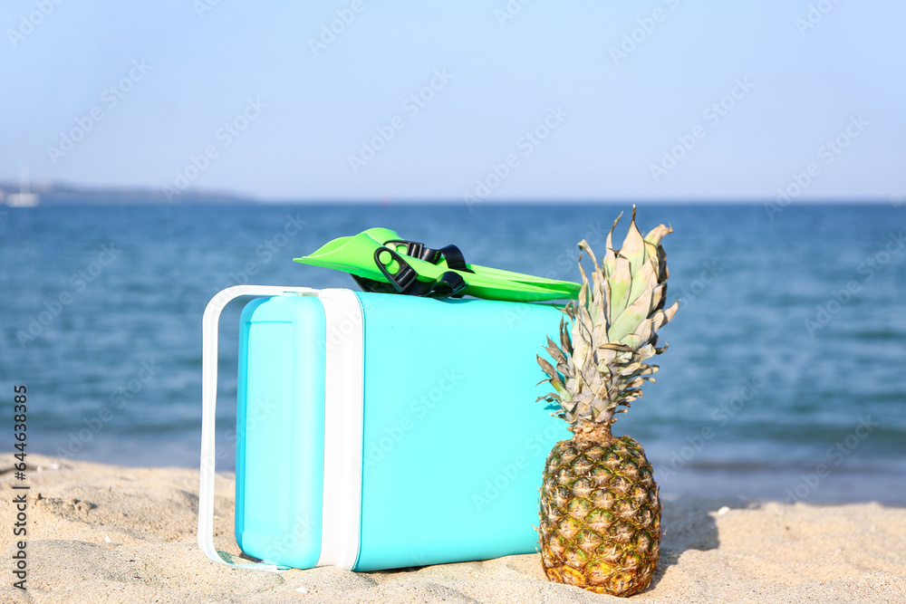 Beach cooler, flippers and pineapple on sand