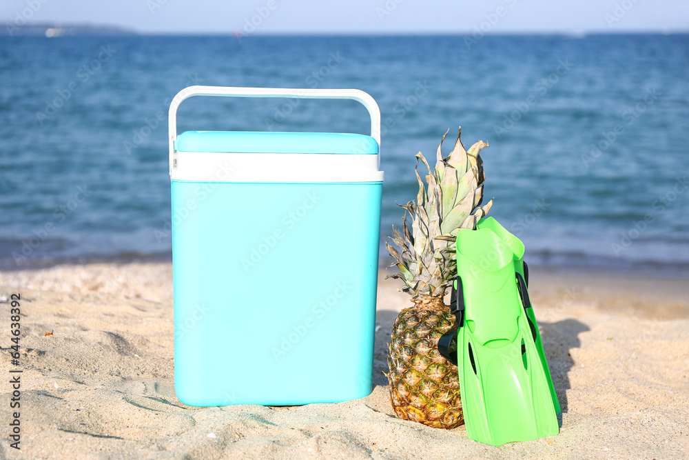 Beach cooler, flippers and pineapple on sand