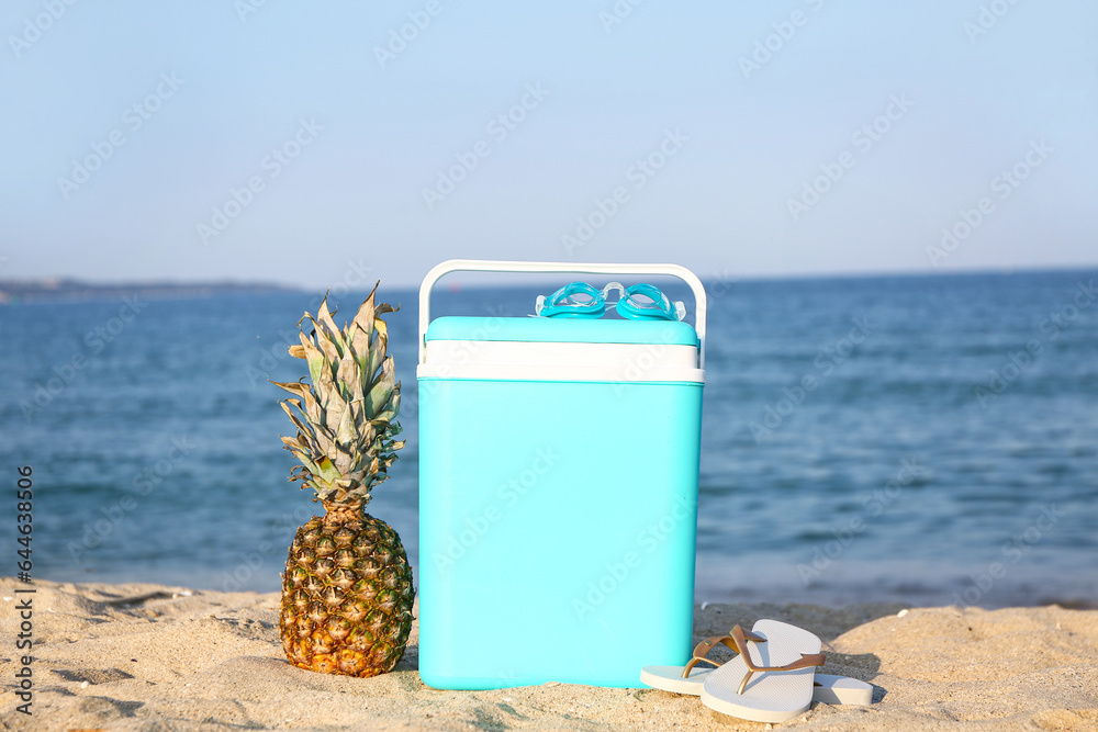 Beach cooler, accessories and pineapple on sand