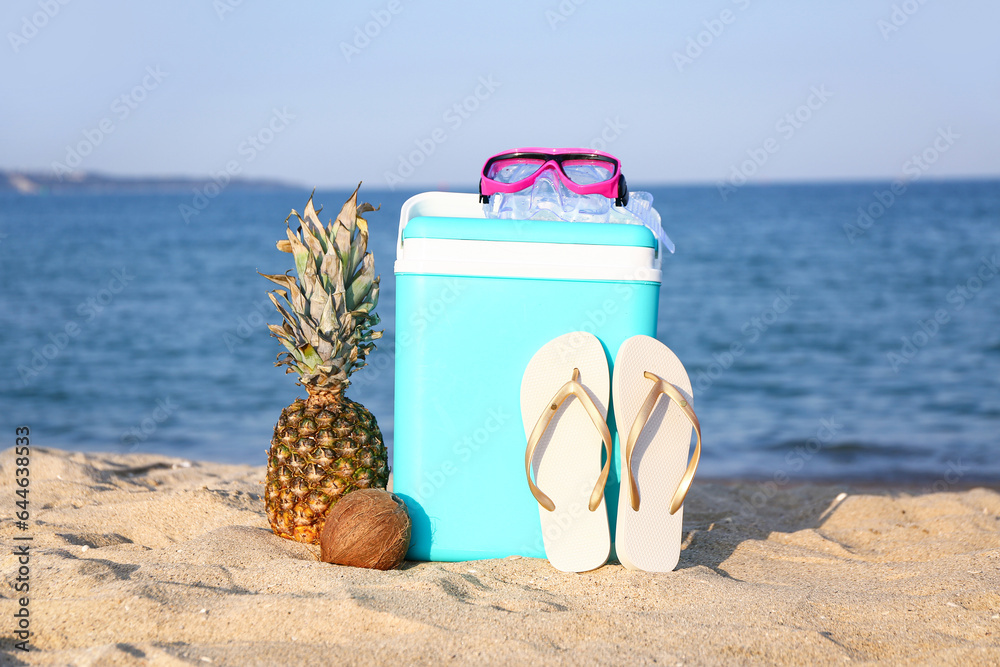 Beach cooler, accessories and fruits on sand