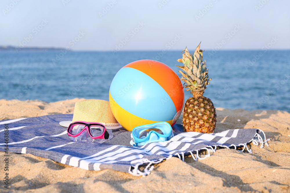 Towel with beach accessories and ripe pineapple on sea beach