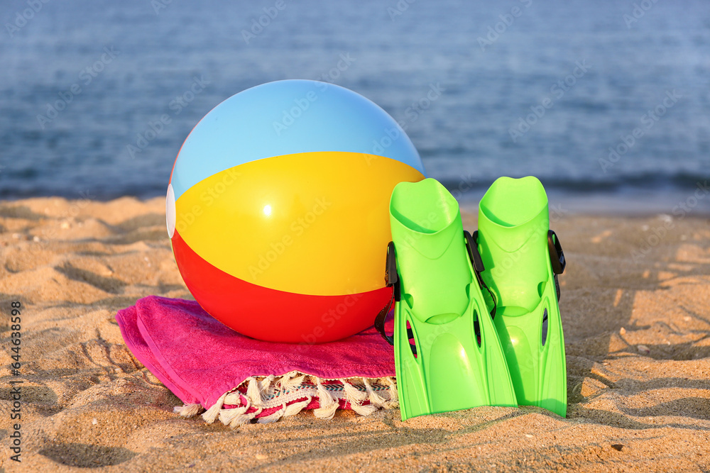 Inflatable ball, flippers and towel on sea beach