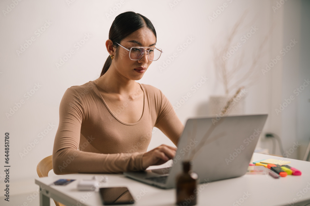 Asian person using laptop computer, sitting in living room in apartment. attractive man is working f