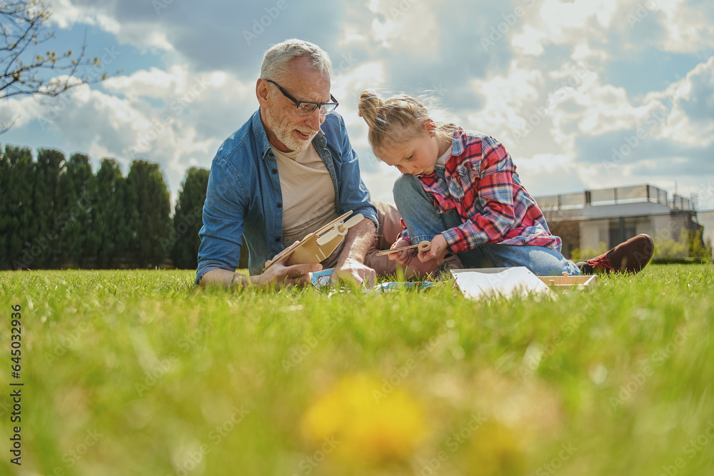 Focused child holding toy while playing with her grey haired grandfather at grassy lawn