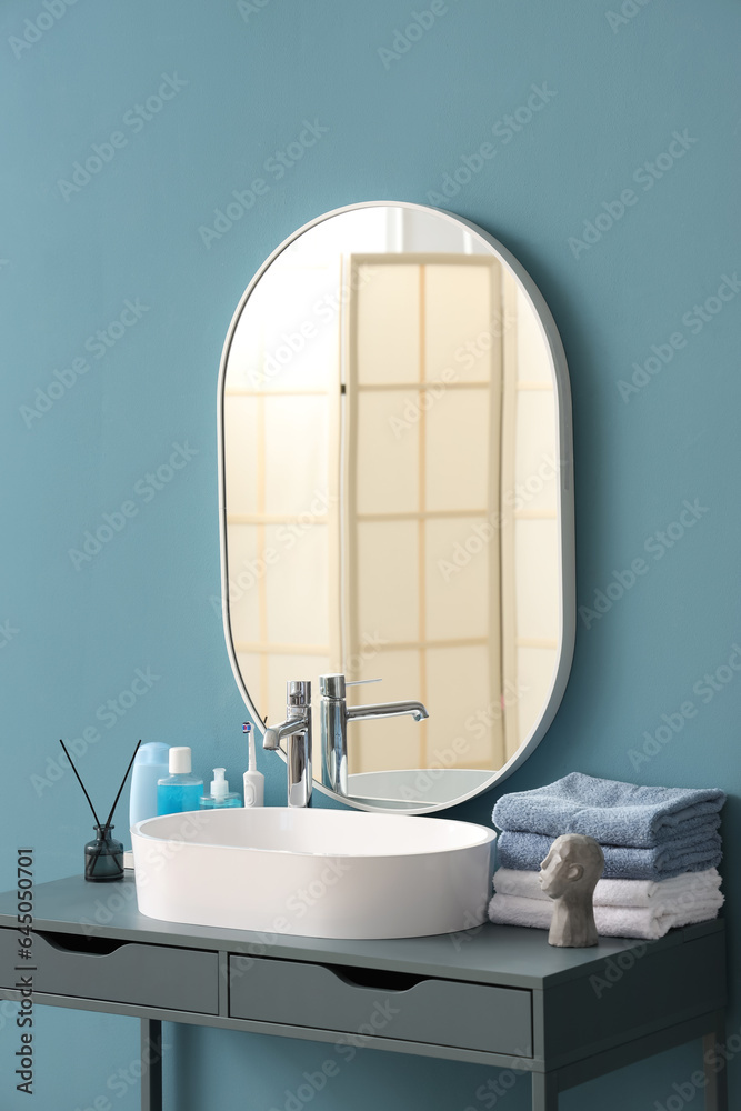 White sink with bath accessories on table near color wall