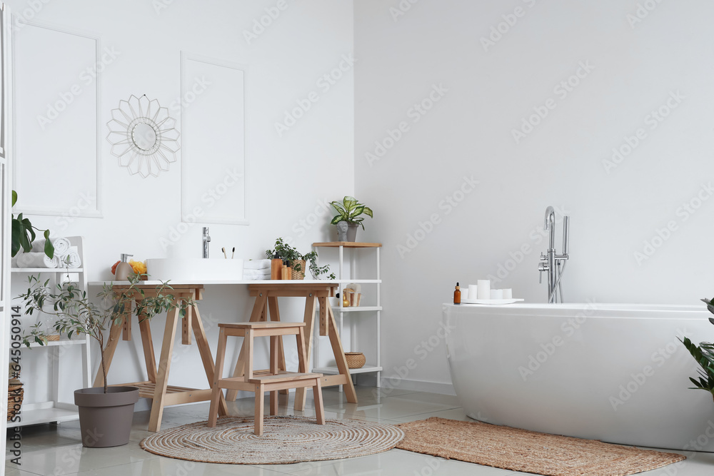 Interior of light bathroom with white sink, bathtub and houseplants