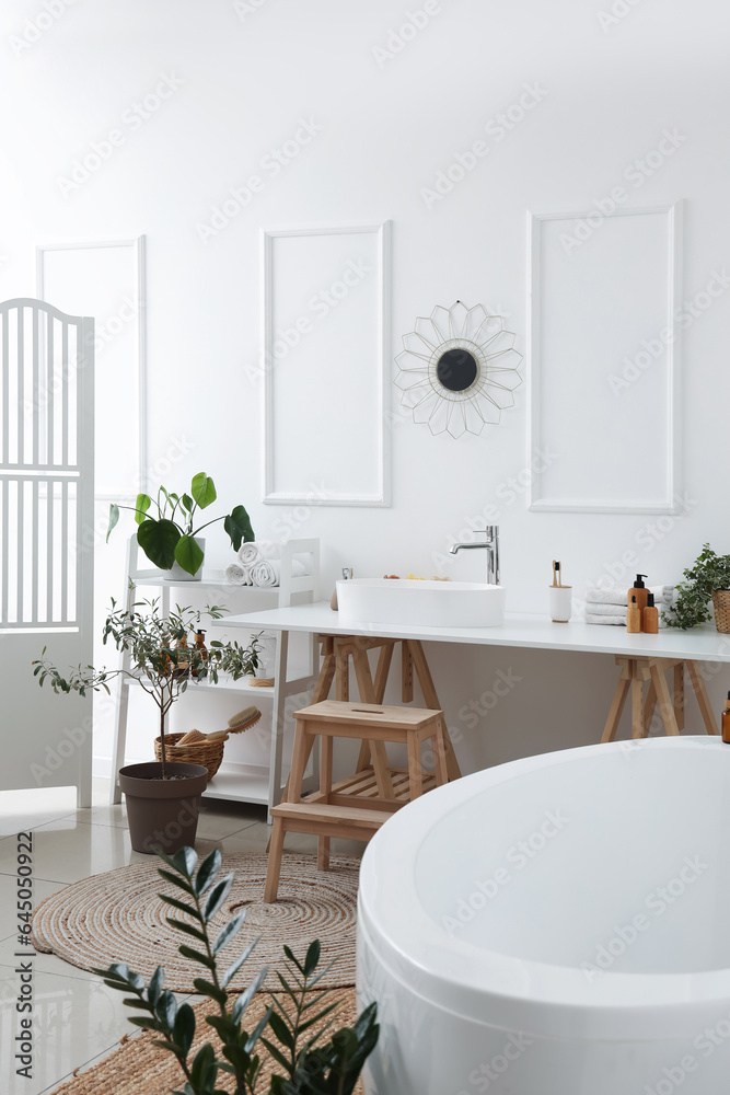 Interior of light bathroom with white sink, bathtub and houseplants