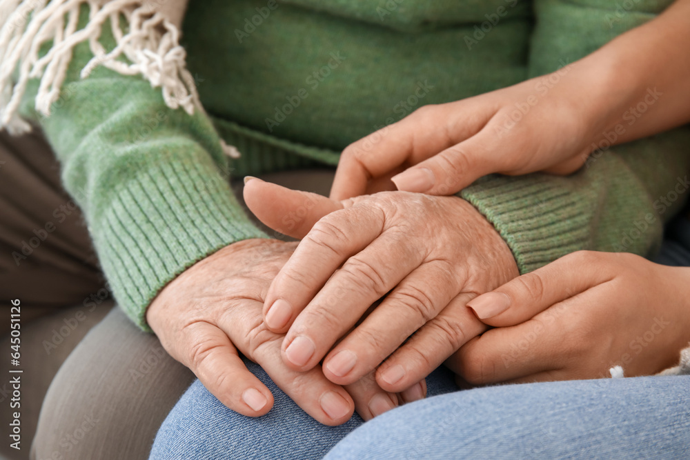 Senior woman with her granddaughter holding hands at home, closeup