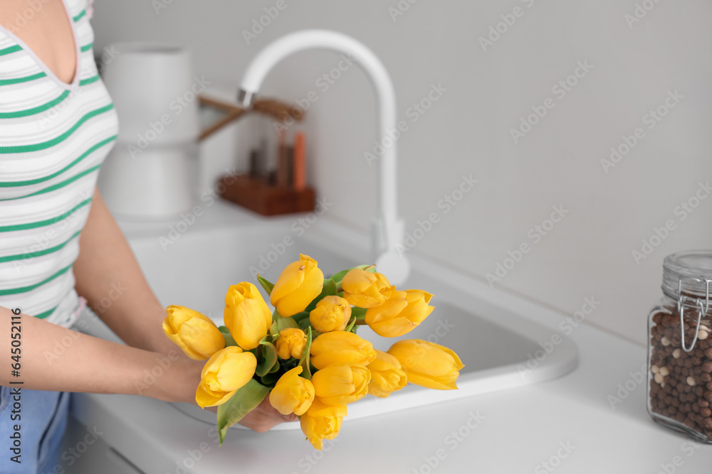 Woman holding bouquet of yellow tulip flowers near kitchen sink