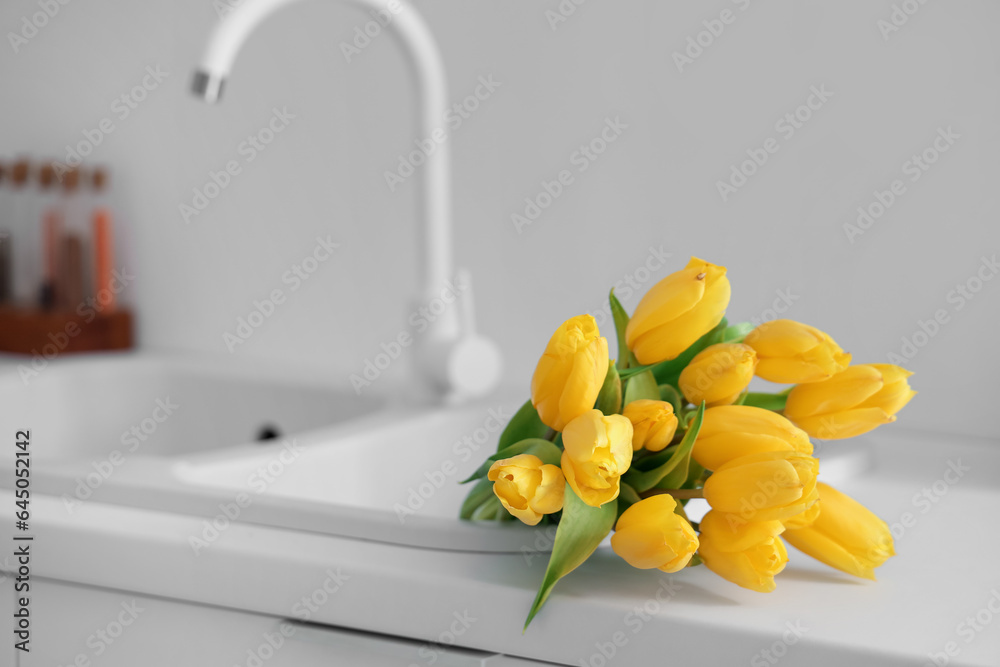 Bouquet of yellow tulip flowers on white kitchen counter near sink