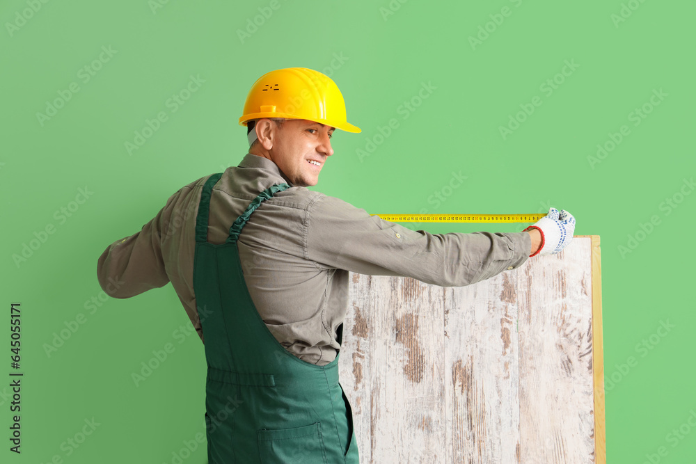 Mature builder measuring wooden plank near green wall, back view