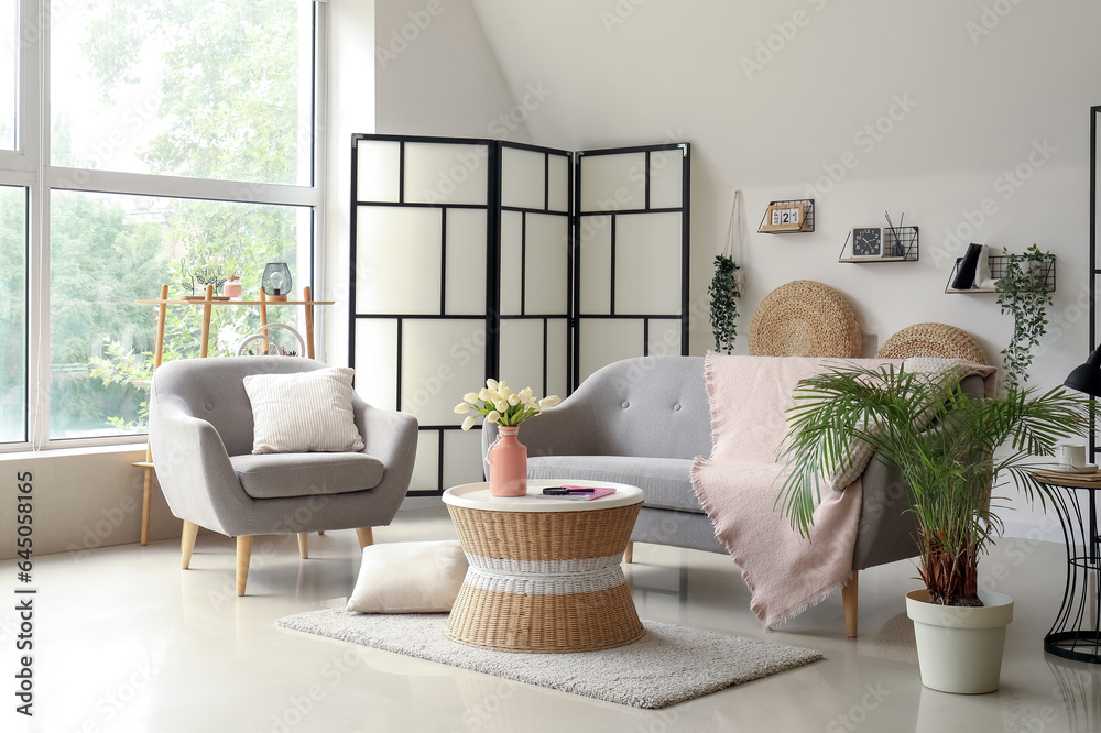 Interior of light living room with comfortable grey sofa, armchair and coffee table