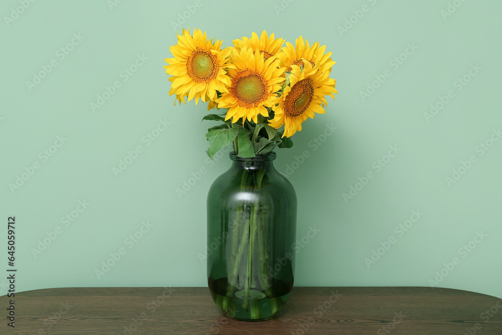 Vase with sunflowers on shelf near green wall