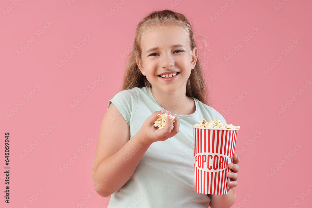 Happy little girl with bucket of popcorn on pink background