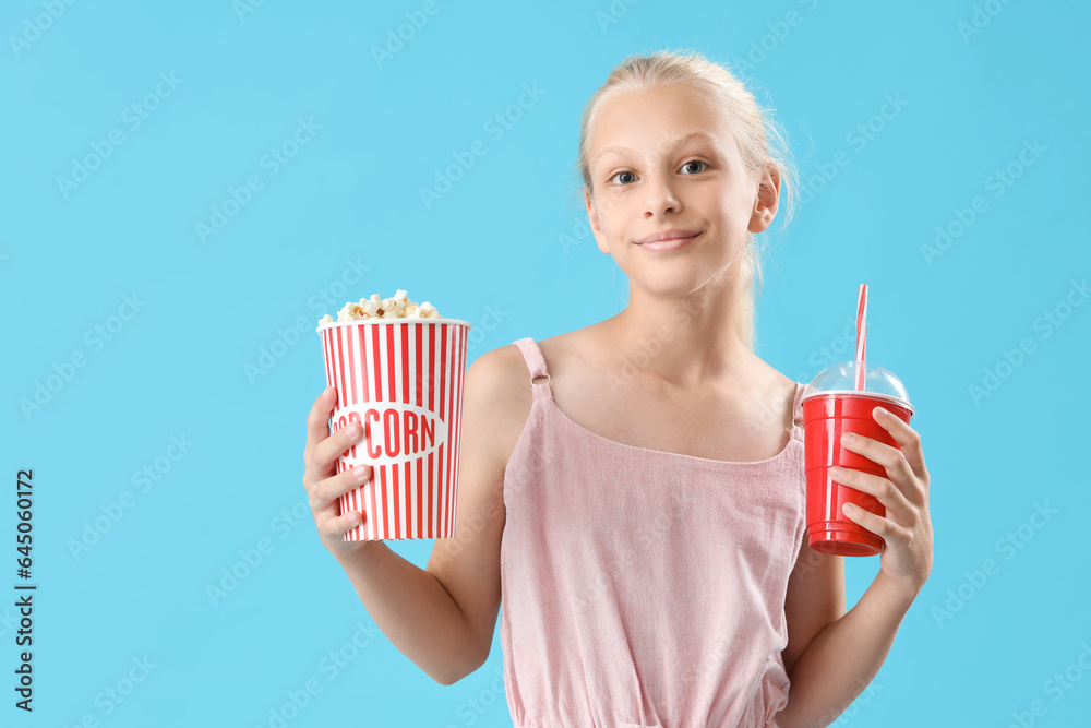 Happy girl with popcorn bucket and cup of cola on blue background