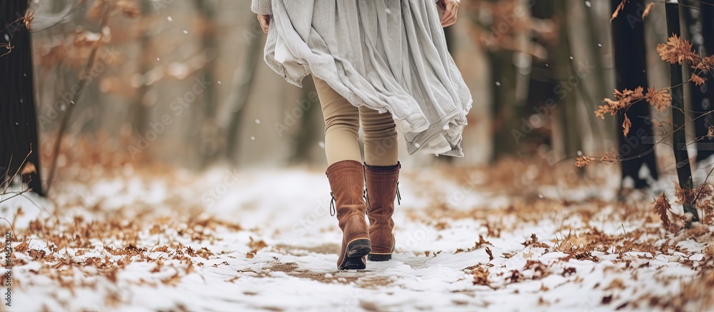 close up woman feet wearing boots walking in early winter park with dry crispy leave and snow flakes