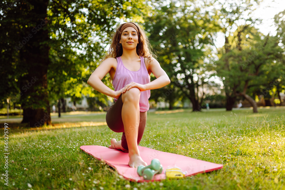 Fitness woman doing yoga, sports exercises in the park. Athletic woman sitting on a mat outdoors on 