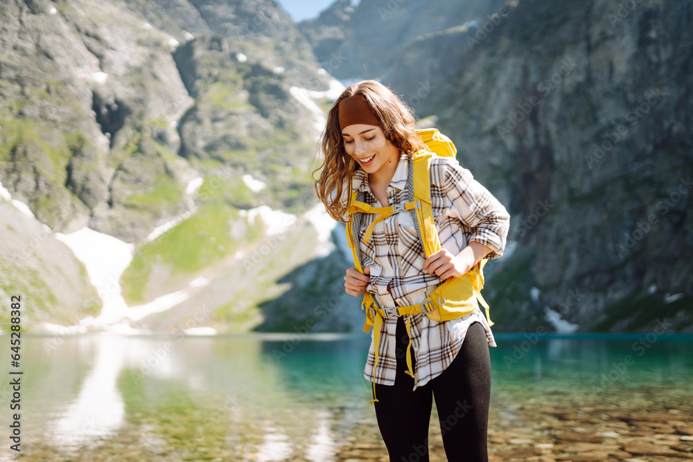 A smiling female traveler with a yellow hiking backpack against the backdrop of a turquoise lake amo