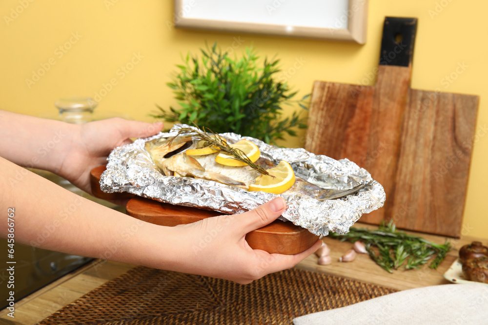 Female hands with tasty baked fish in kitchen, closeup