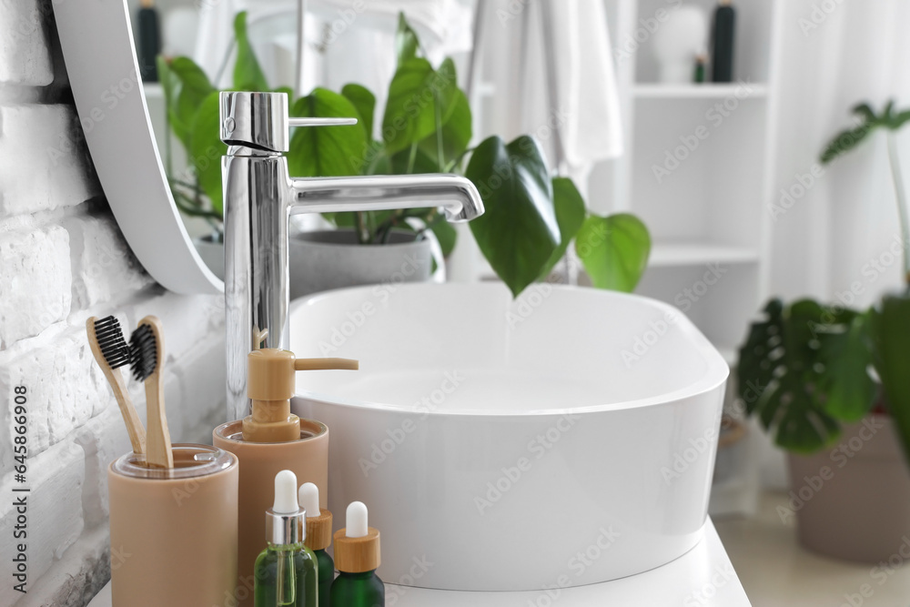 White sink with bath accessories  on table and houseplants in bathroom, closeup