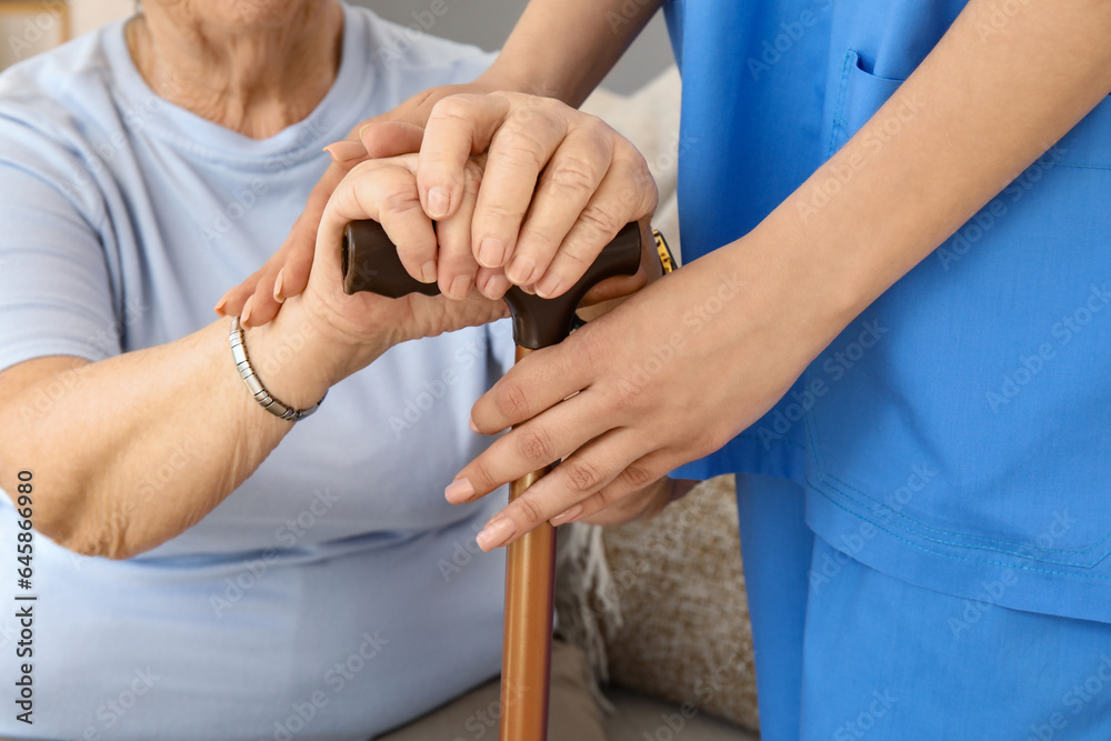 Senior woman with walking stick and female caregiver at home, closeup