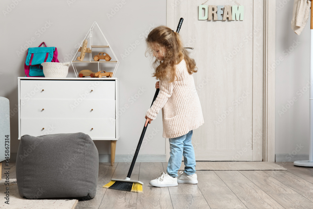 Cute little girl sweeping floor with broom at home