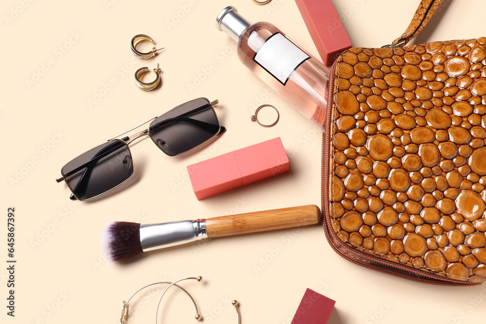 Cosmetic bag with sunglasses, makeup products and accessories on pale orange background