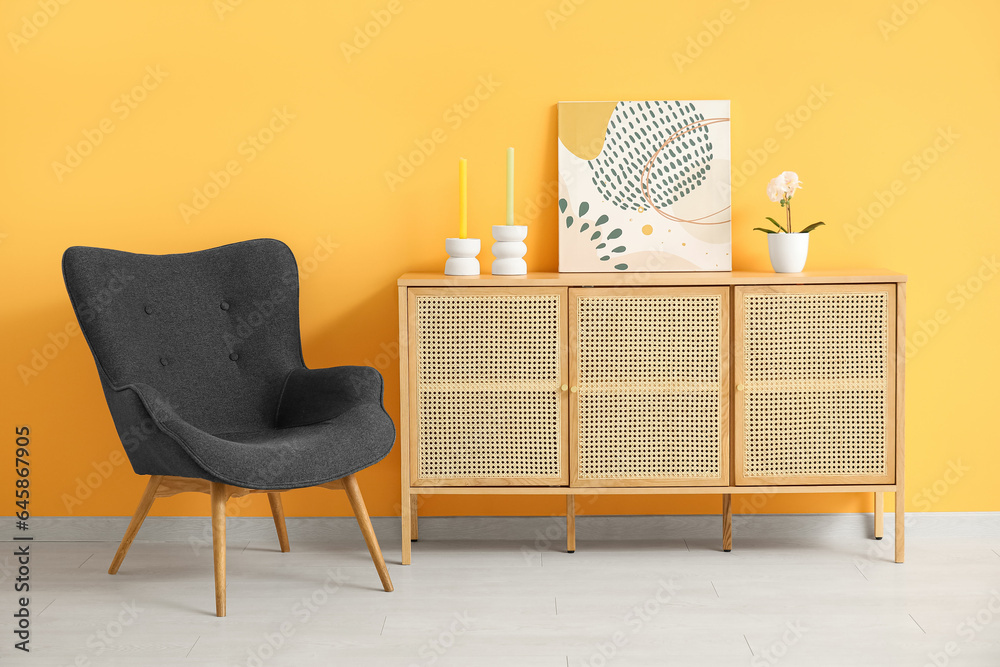 Dark grey armchair with dresser, painting and candles near orange wall