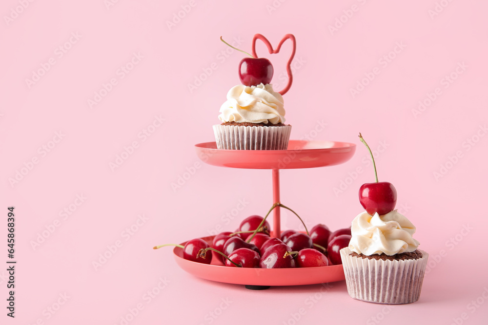 Stand with tasty cherry cupcakes on pink background