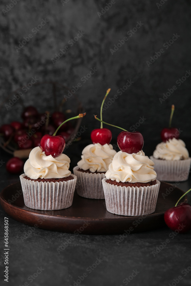 Plate with tasty cherry cupcakes on black background