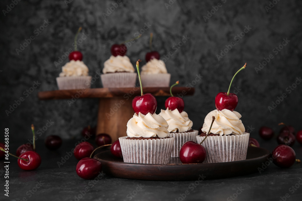 Plate with tasty cherry cupcakes on black background