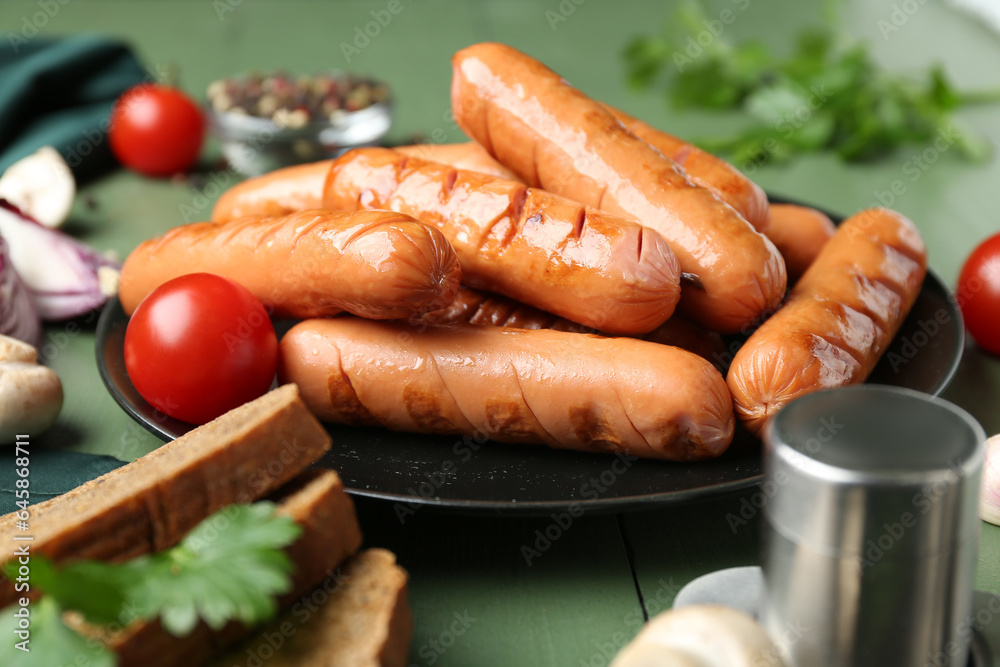 Plate with tasty grilled sausages and vegetables on green wooden table, closeup