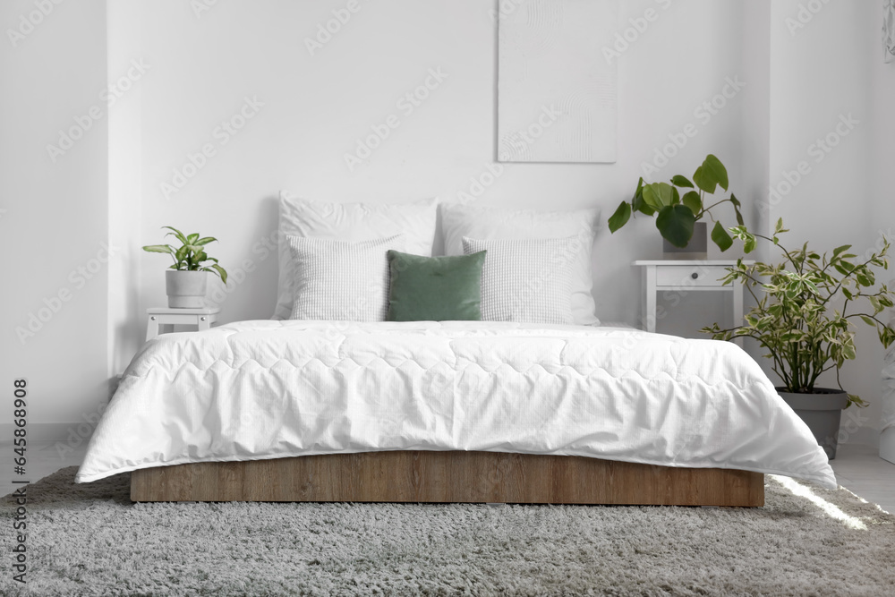 Cozy bed with white blanket and pillows in interior of light bedroom