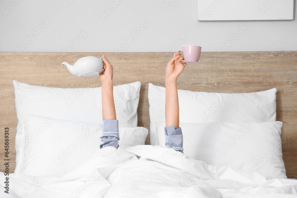 Morning of young woman with cup and teapot in bed