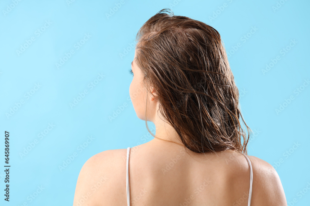 Young woman after washing hair on blue background, back view