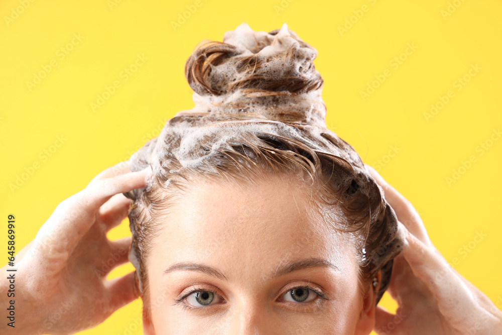 Young woman washing hair on yellow background, closeup