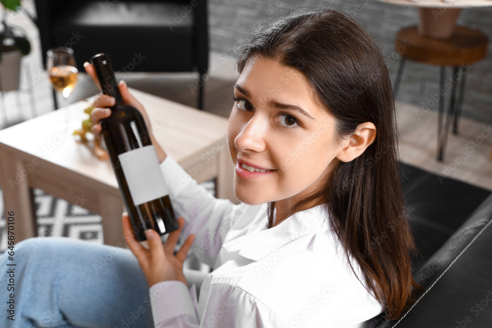 Young woman with bottle of wine sitting at home, closeup