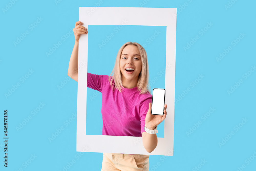 Young beautiful happy woman with frame and mobile phone on blue background