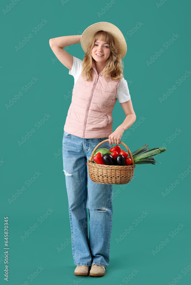 Happy young female farmer with wicker basket full of different ripe vegetables on green background