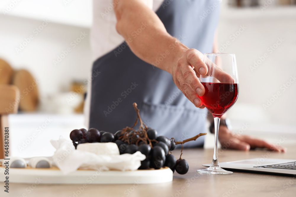 Mature man with glass of red wine in kitchen, closeup