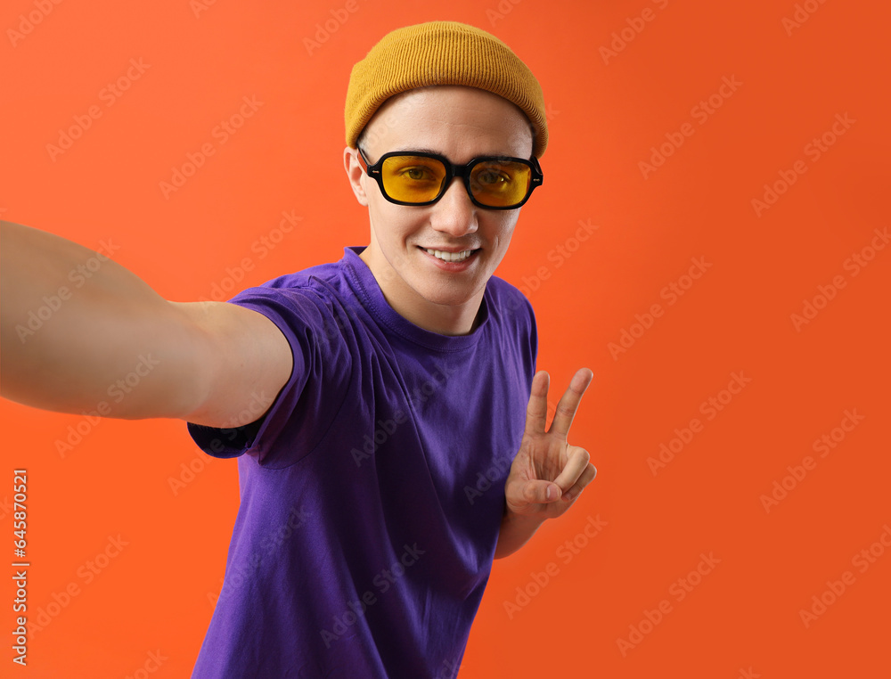 Young man in sunglasses taking selfie on red background, closeup