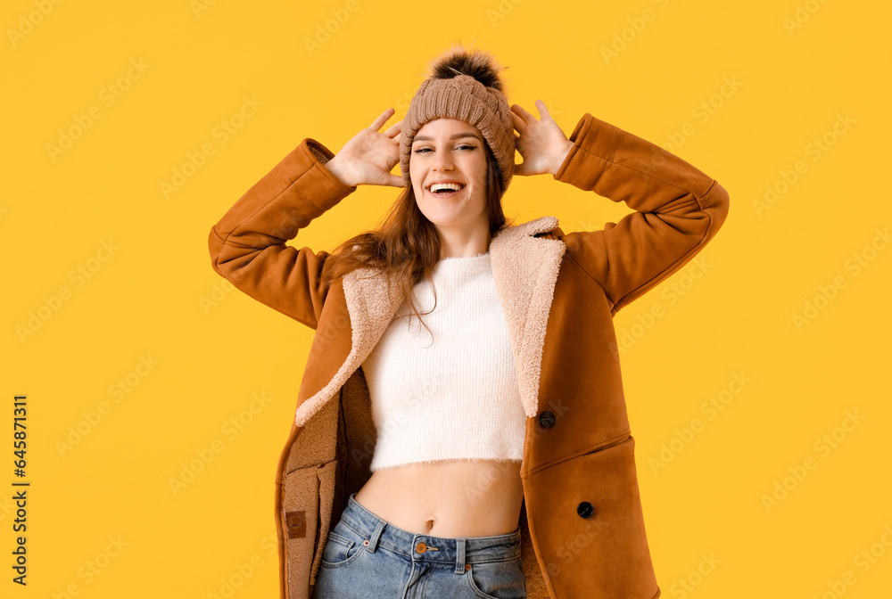 Young woman in winter clothes on yellow background