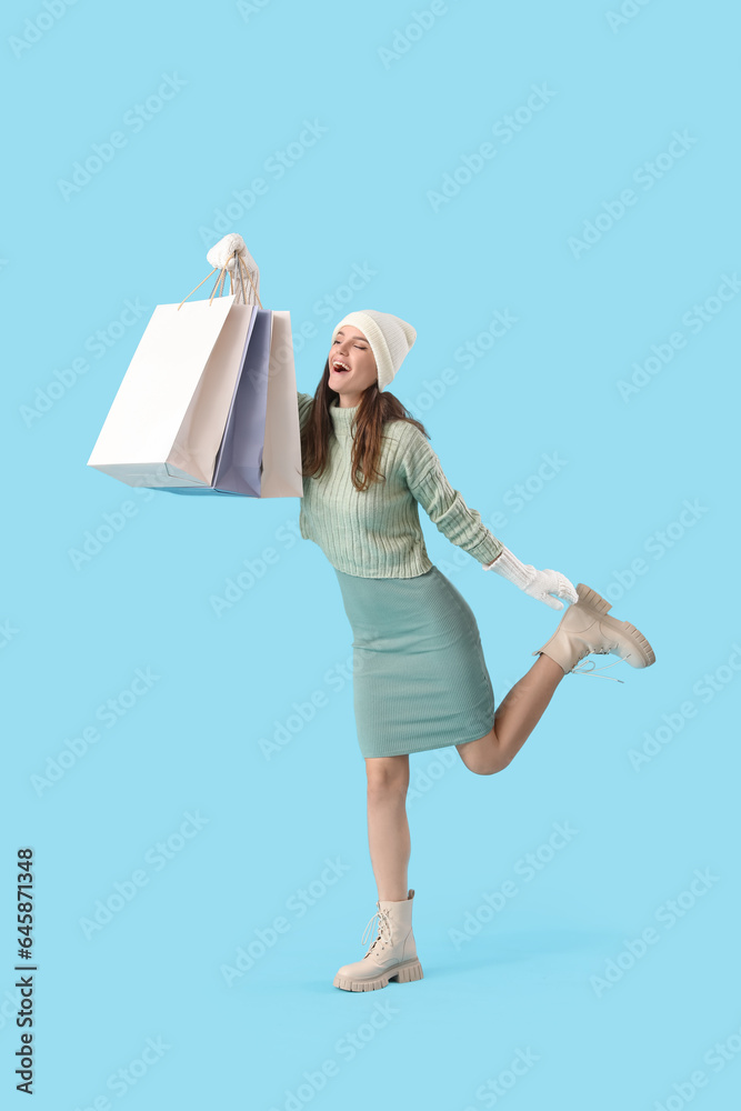 Young woman in winter clothes with shopping bags on blue background