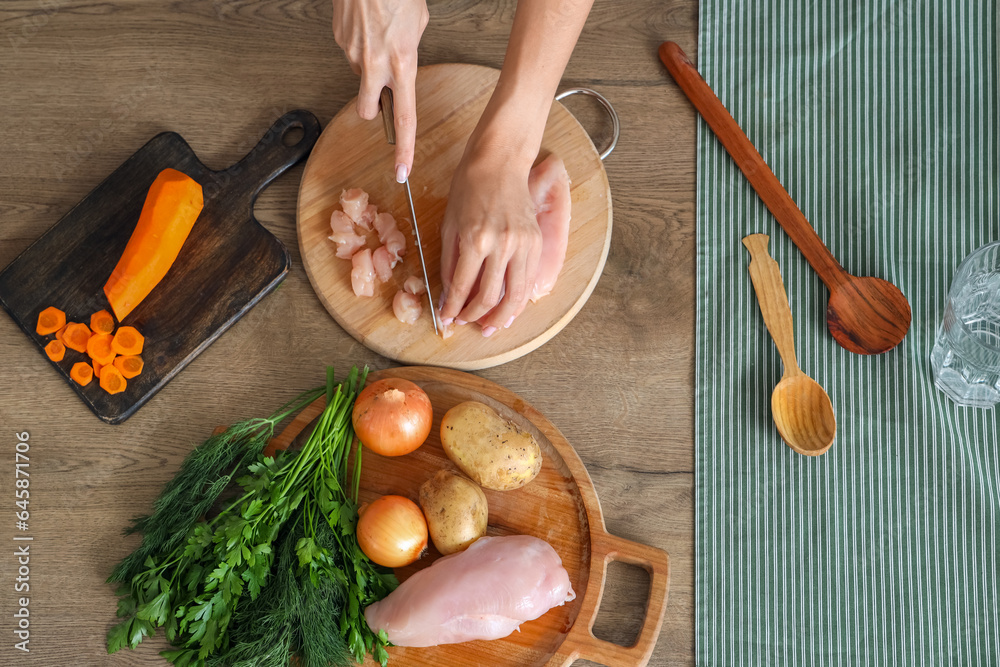 Young woman cutting chicken fillet for soup in kitchen, top view